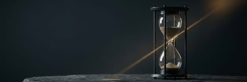Un reloj de arena atravesado por un rayo de luz cálida en una sala oscura