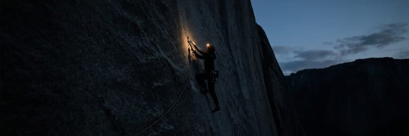 Un escalador con linterna frontal subiendo una pared de roca al anochecer