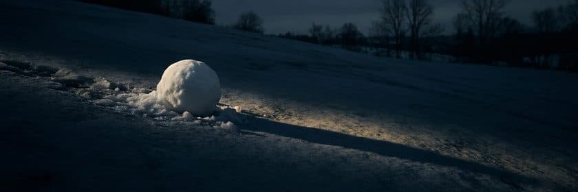 Una bola de nieve que crece mientras rueda por una ladera nevada al anochecer