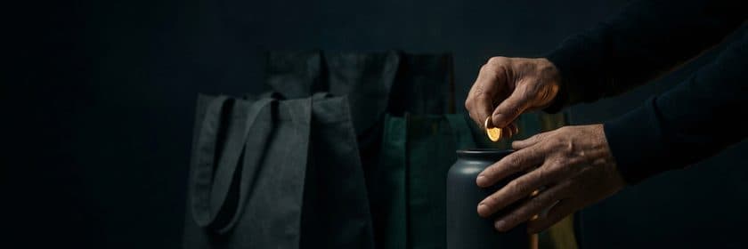Una mano dejando una moneda dentro de un tarro, junto a bolsas de compras