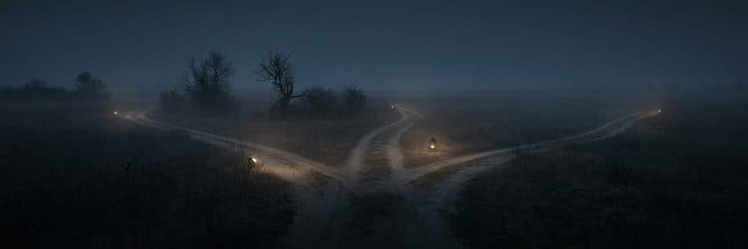 Tres caminos que se separan desde un mismo punto en un campo con neblina al anochecer, cada uno con su luz