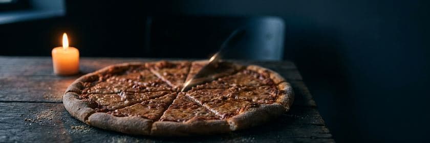 Una pizza cortada en muchas porciones sobre una mesa de madera, junto a una vela encendida
