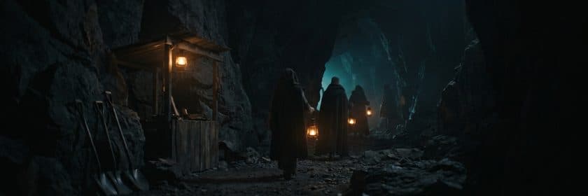 Personas con faroles entrando a una mina dentro de una caverna, junto a palas apoyadas en la roca