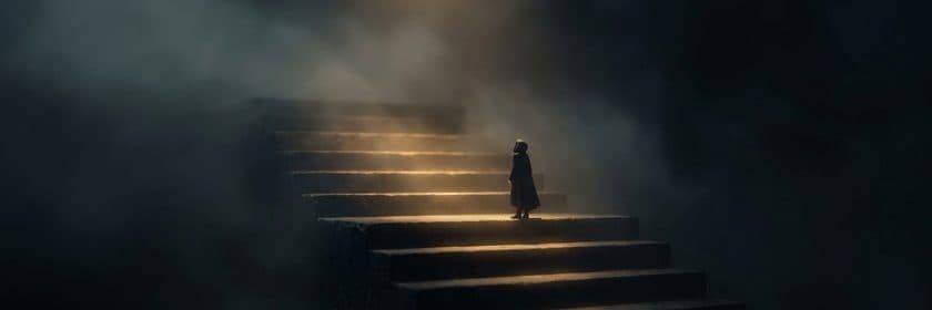 Una pequeña figura subiendo una escalera de piedra entre la niebla, iluminada desde arriba