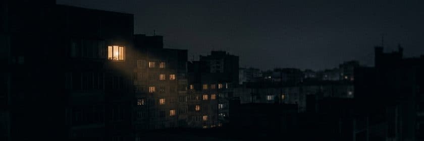 Un edificio de departamentos de noche con una sola ventana iluminada más fuerte que el resto