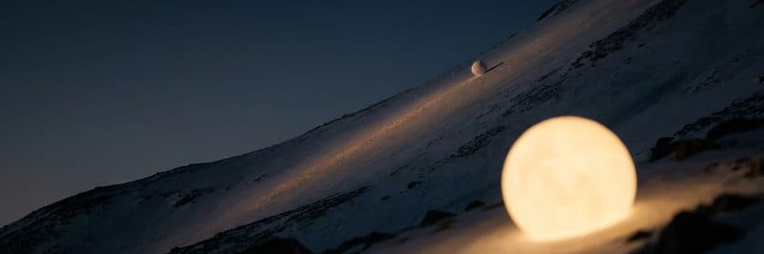 Una bola de nieve luminosa que crece mientras rueda por una ladera nevada de noche