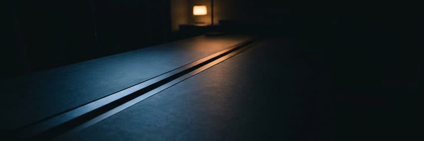 Dos líneas metálicas paralelas muy juntas sobre una superficie oscura, con una lámpara encendida al fondo