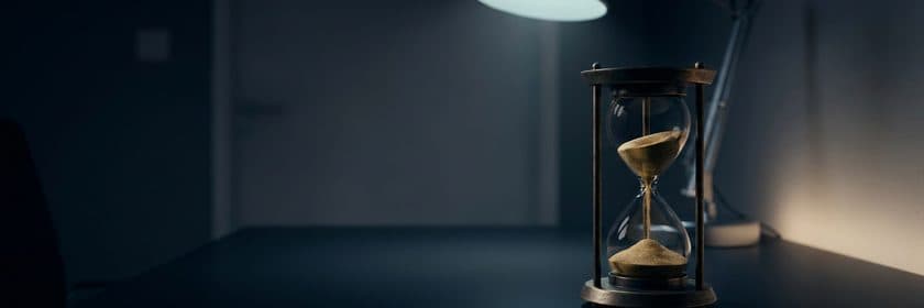 Un reloj de arena con la arena cayendo, junto a una lámpara en una habitación oscura