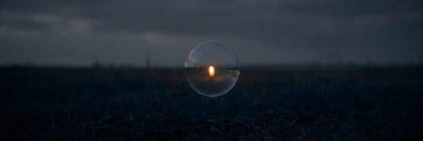 Una burbuja de jabón flotando sobre un campo oscuro de noche, con una luz cálida reflejada adentro