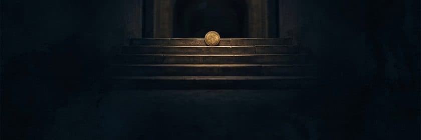 Una moneda dorada apoyada en el primer escalón de una escalera de piedra, en la penumbra